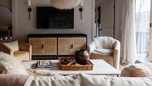 Sala de estar con televisor, mobiliario de mimbre y un ventanal grande.