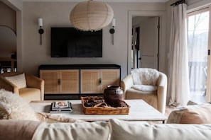 Un salon avec un téléviseur, des meubles en osier et une grande fenêtre.