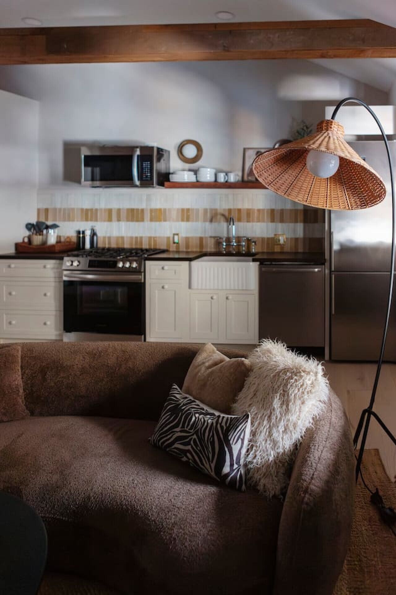 Un salon chaleureux avec un canapé marron, un coussin à motifs zébrés et une lampe de sol en osier.