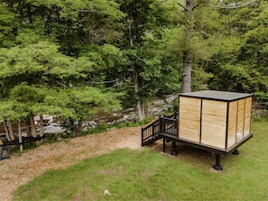 A wooden structure with a black railing, situated on a grassy slope with trees in the background.