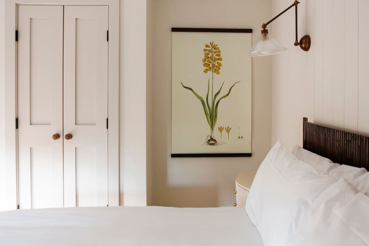Ein Schlafzimmer mit einem Bett, einer Wandlampe und einem botanischen Druck in einem Rahmen.