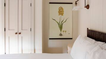 Ein Schlafzimmer mit einem Bett, einer Wandlampe und einem botanischen Druck in einem Rahmen.