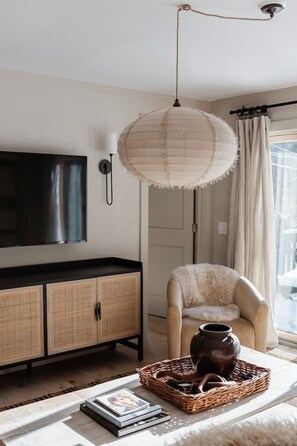 A living room with a flat-screen TV, a wicker basket with a vase, and a chair.