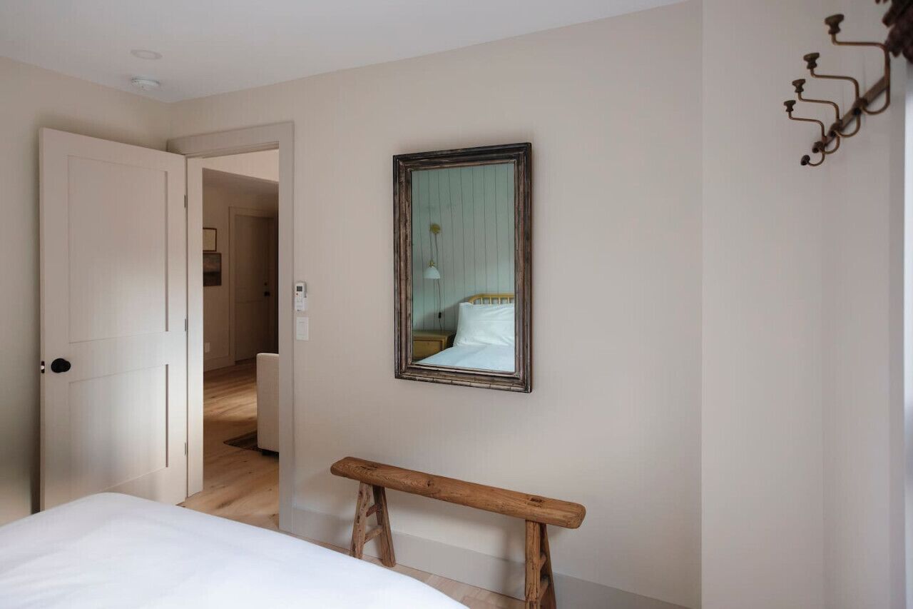 A bedroom with a bed, a wooden bench, a mirror, and a door leading to another room.