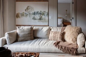 Un salon avec un canapé, des coussins, une couverture, un tableau au mur et une lampe.