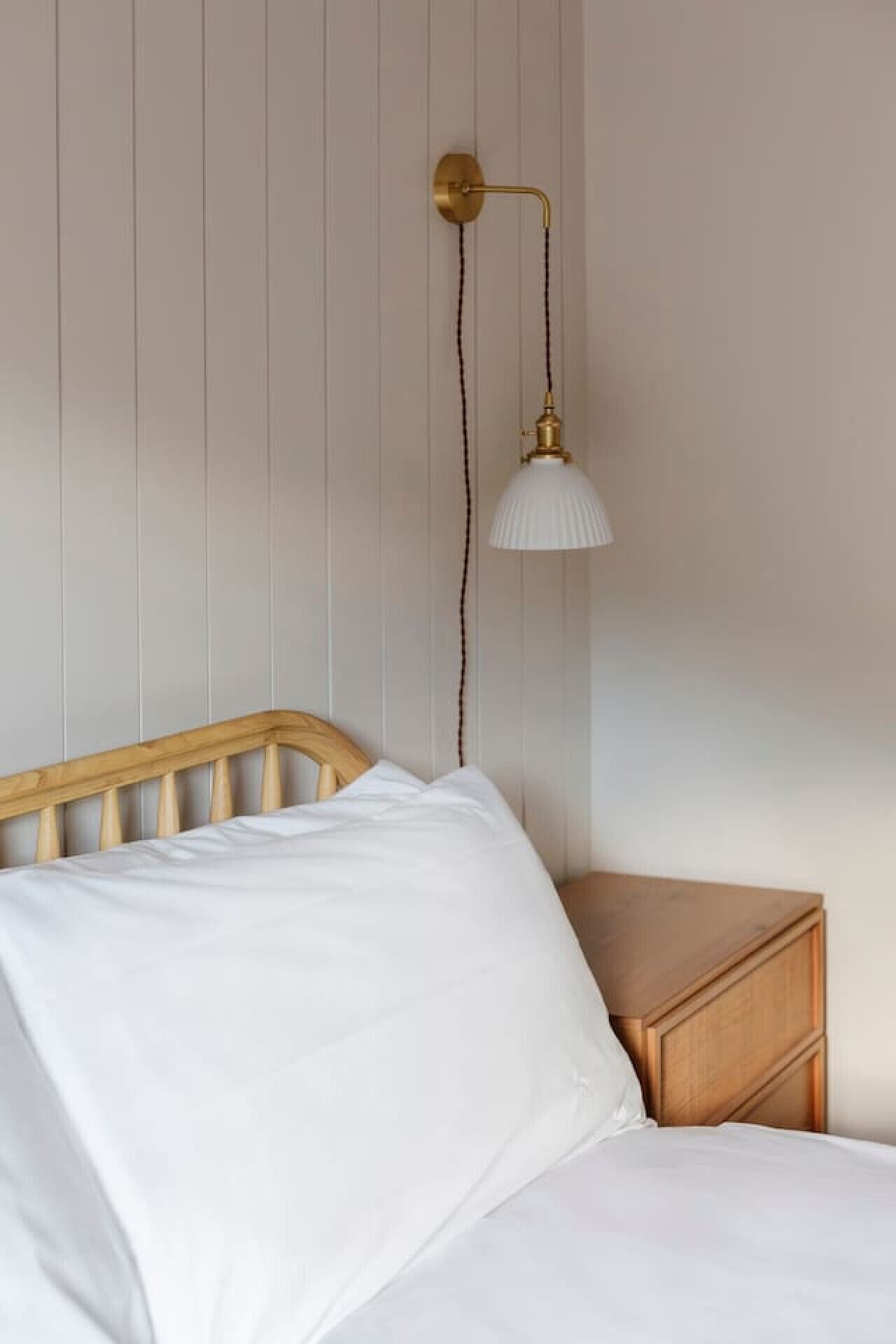 Ein Bett mit weißer Bettwäsche, einem hölzernen Kopfteil und einem Nachttisch mit Lampe.
