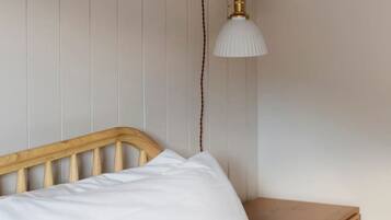 Ein Bett mit weißer Bettwäsche, einem hölzernen Kopfteil und einem Nachttisch mit Lampe.