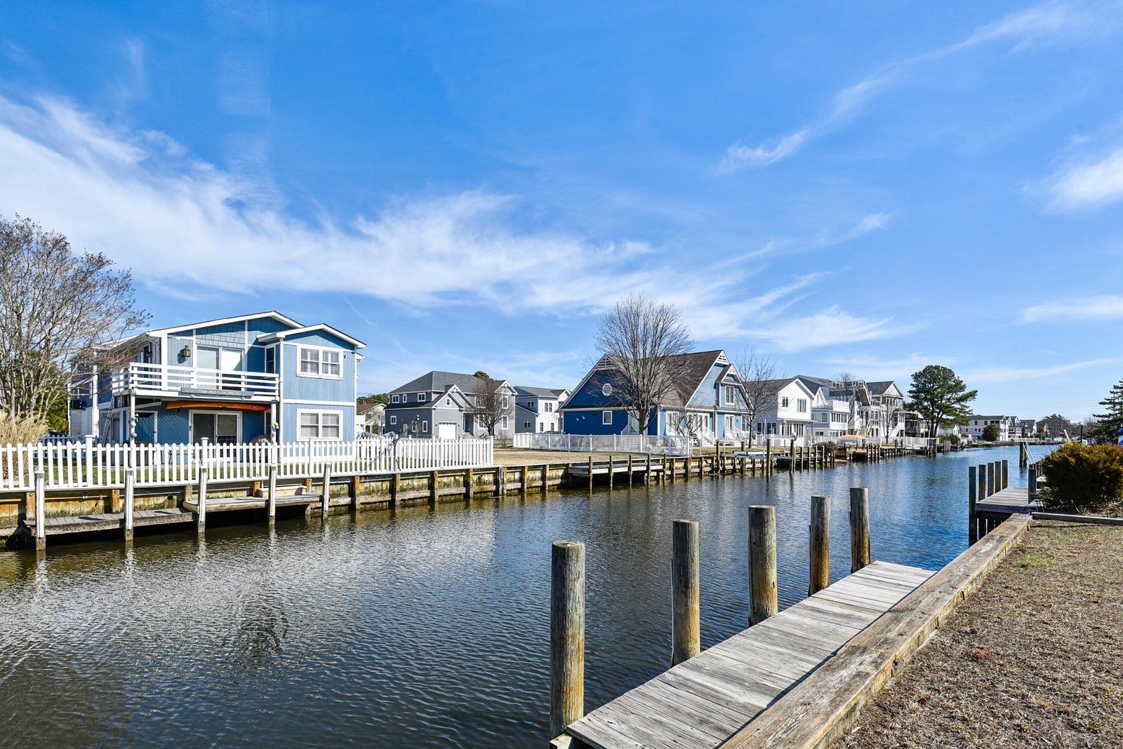 A waterfront property with a dock, a white picket fence, and houses with a blue facade.