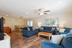 A living room with a ceiling fan, a dining area with a table and chairs, and a kitchen area with cabinets. - Captivating Canal Views at This Bayside Getaway in Bethany Beach! (Bethany Beach)