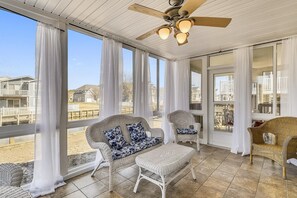 A covered outdoor seating area with wicker furniture, large windows, and a ceiling fan. - Captivating Canal Views at This Bayside Getaway in Bethany Beach! (Bethany Beach)
