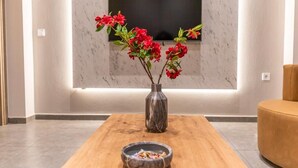 Ein modernes Wohnzimmer mit Marmorwand, Flachbildfernseher, Couchtisch aus Holz, einer Vase mit roten Blumen und einer Schale mit Snacks.