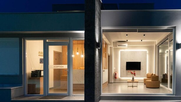 Ein moderner Hotelaufgang mit Glastüren, einer Rezeption und einer Sitzecke mit Fernseher.