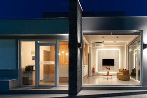 Una entrada de hotel moderna con puertas de cristal, una zona de recepción y un salón con televisor y asientos.
