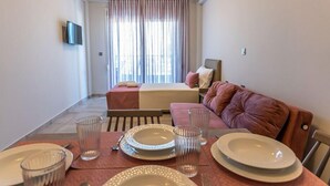 Ein Hotelzimmer mit einem Bett, einem Sofa, einem Esstisch mit Tellern und Gläsern sowie einem an der Wand befestigten Fernseher.