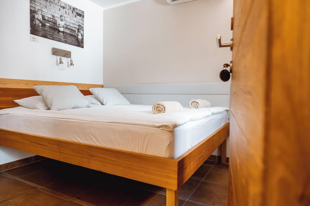 Un lit bien fait, avec du linge de lit blanc et des serviettes pliées, une tête de lit en bois et un luminaire fixé au mur.