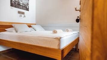A neatly made bed with white linens and rolled towels, a wooden headboard, and a wall-mounted light fixture.