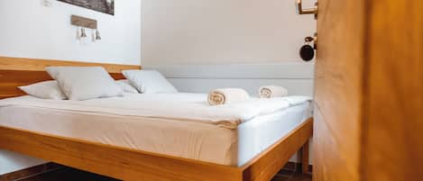 A neatly made bed with white linens and rolled towels, a wooden headboard, and a wall-mounted light fixture.