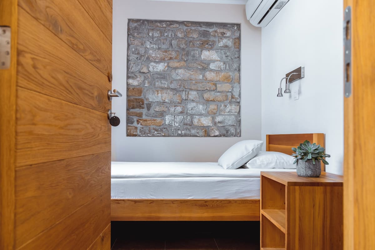 Une chambre avec un lit en bois, un mur en pierre et une petite plante posée sur une table de chevet.