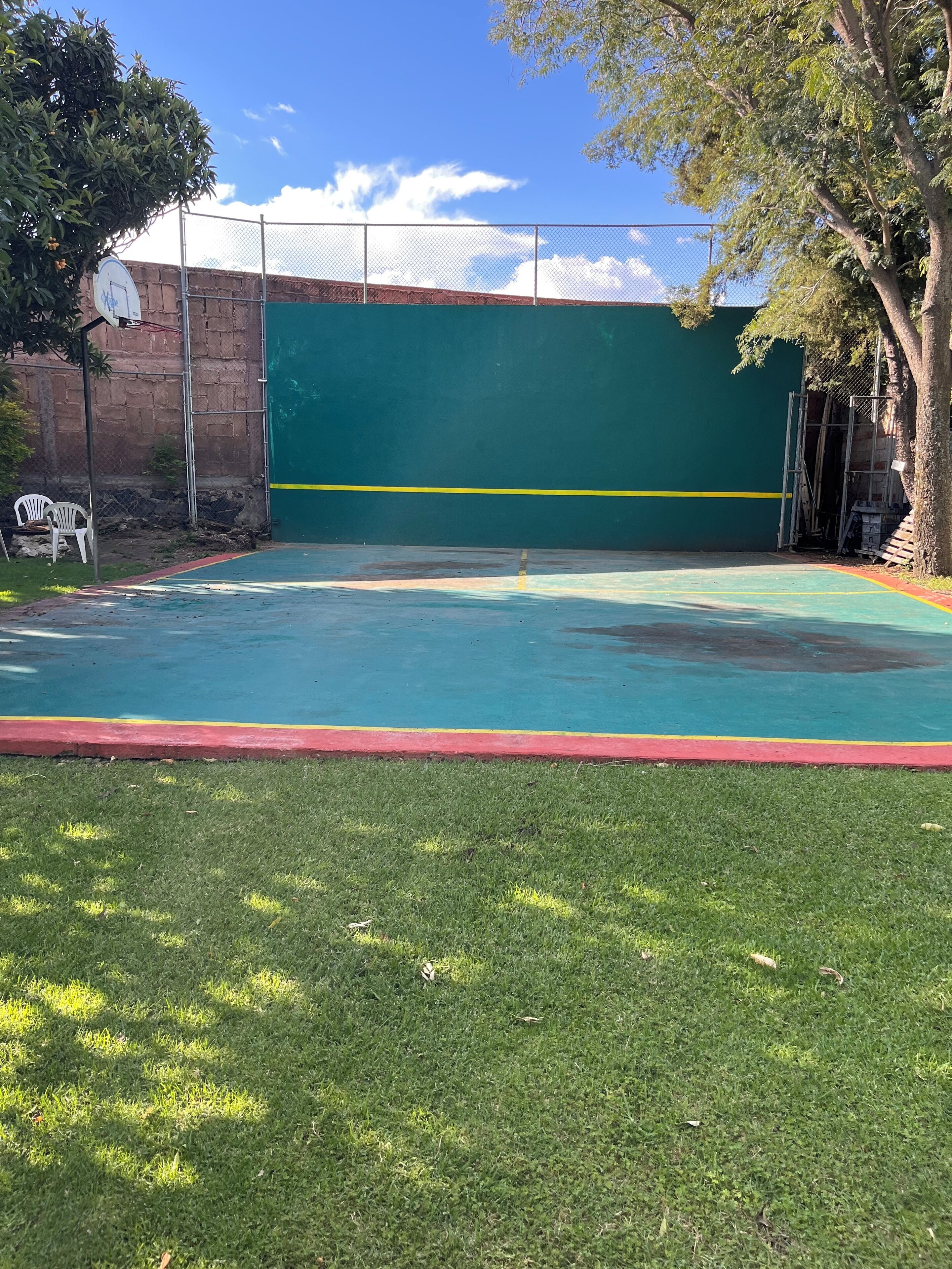 Un terrain de basket avec un mur vert, une bordure rouge et un ciel bleu clair.