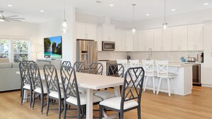 A modern kitchen with white cabinets, a central island with bar stools, and a dining area with a wooden table and chairs. - Sacajawea by the Sea (Port St. Joe)