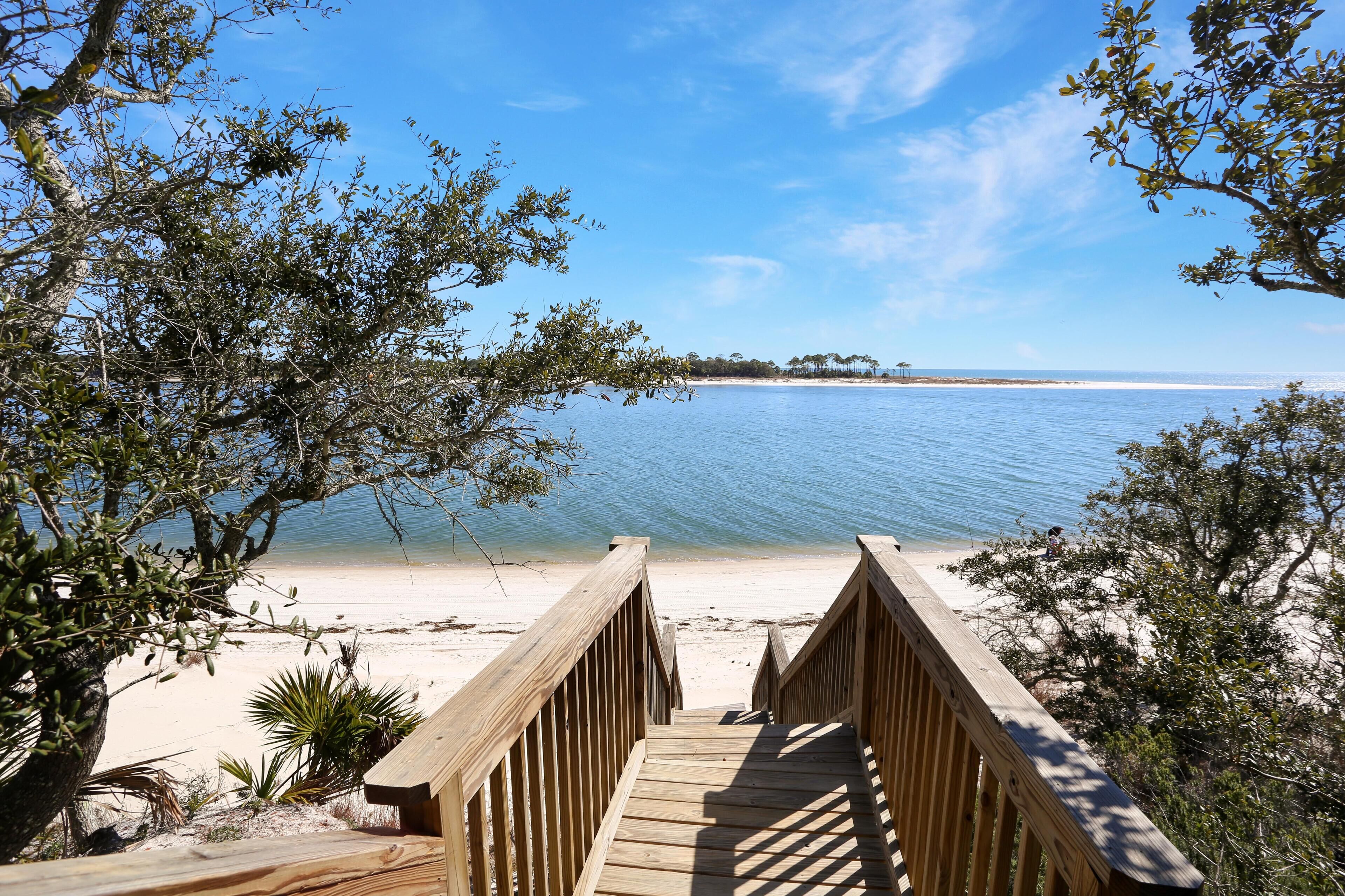 A wooden boardwalk leading to a beach with clear blue water and distant trees.