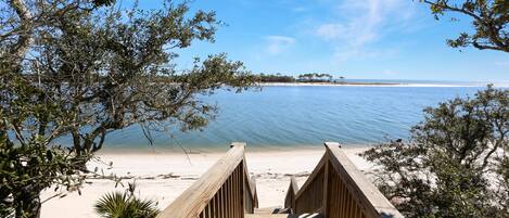 A wooden boardwalk leading to a beach with clear blue water and distant trees.