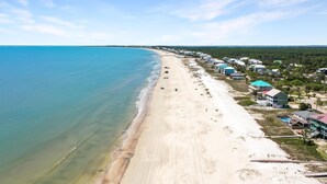 An aerial view of a beachside property with a long sandy beach, clear blue water, and a row of buildings with green roofs. - Sacajawea by the Sea (Port St. Joe)