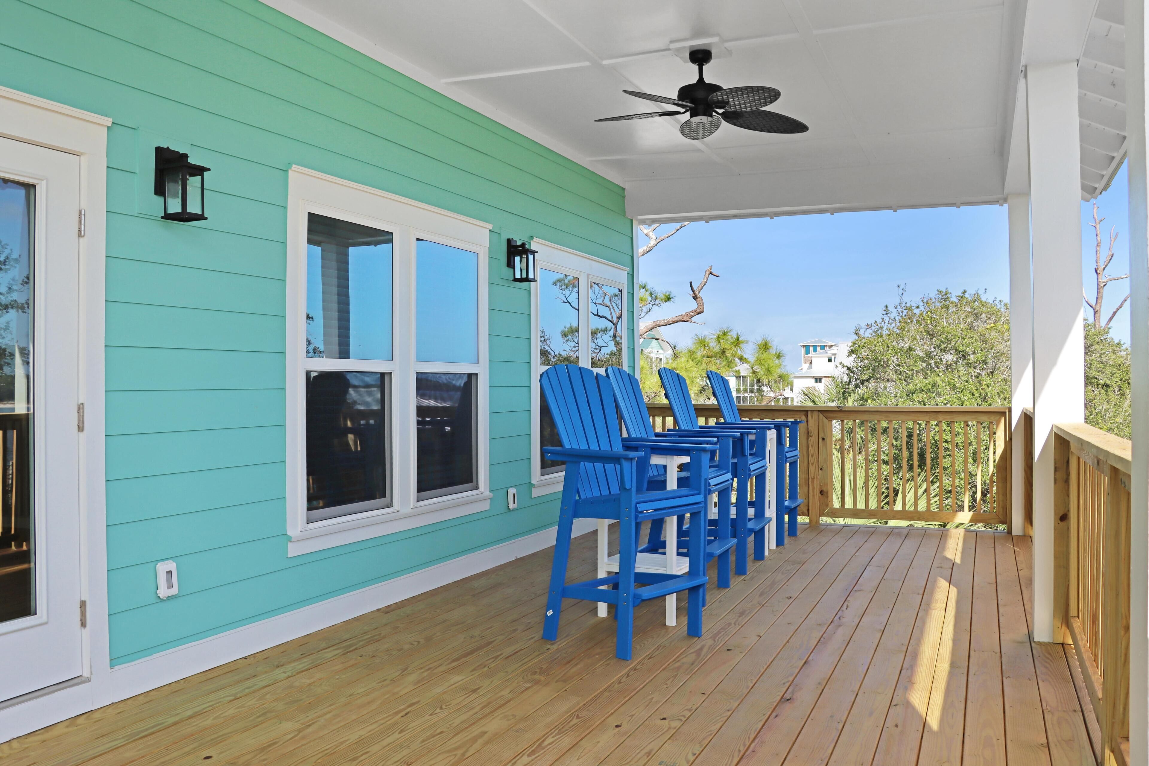 A covered porch with teal siding, a ceiling fan, and blue Adirondack chairs.