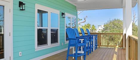 A covered porch with teal siding, a ceiling fan, and blue Adirondack chairs.