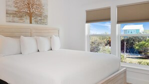 A bedroom with a large bed, white bedding, a wooden headboard, and a window with blinds. - Sacajawea by the Sea (Port St. Joe)