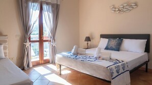 Ein Hotelzimmer mit Bett, Nachttisch, Lampe und Blick ins Freie durch ein mit Vorhängen versehenes Fenster.