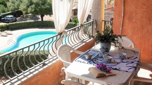 Ein Balkon mit Pool, weißen Stühlen, einem Tisch mit Buch und Blumenvase sowie Blick auf die Umgebung.