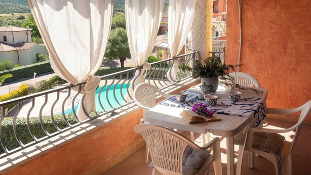 Ein Balkon mit Tisch, Stühlen, einer Topfpflanze und Blick auf einen Swimmingpool.