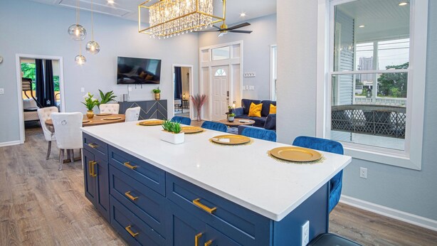 Una cocina moderna con una isla grande, armarios azules, tiradores dorados y una araña.