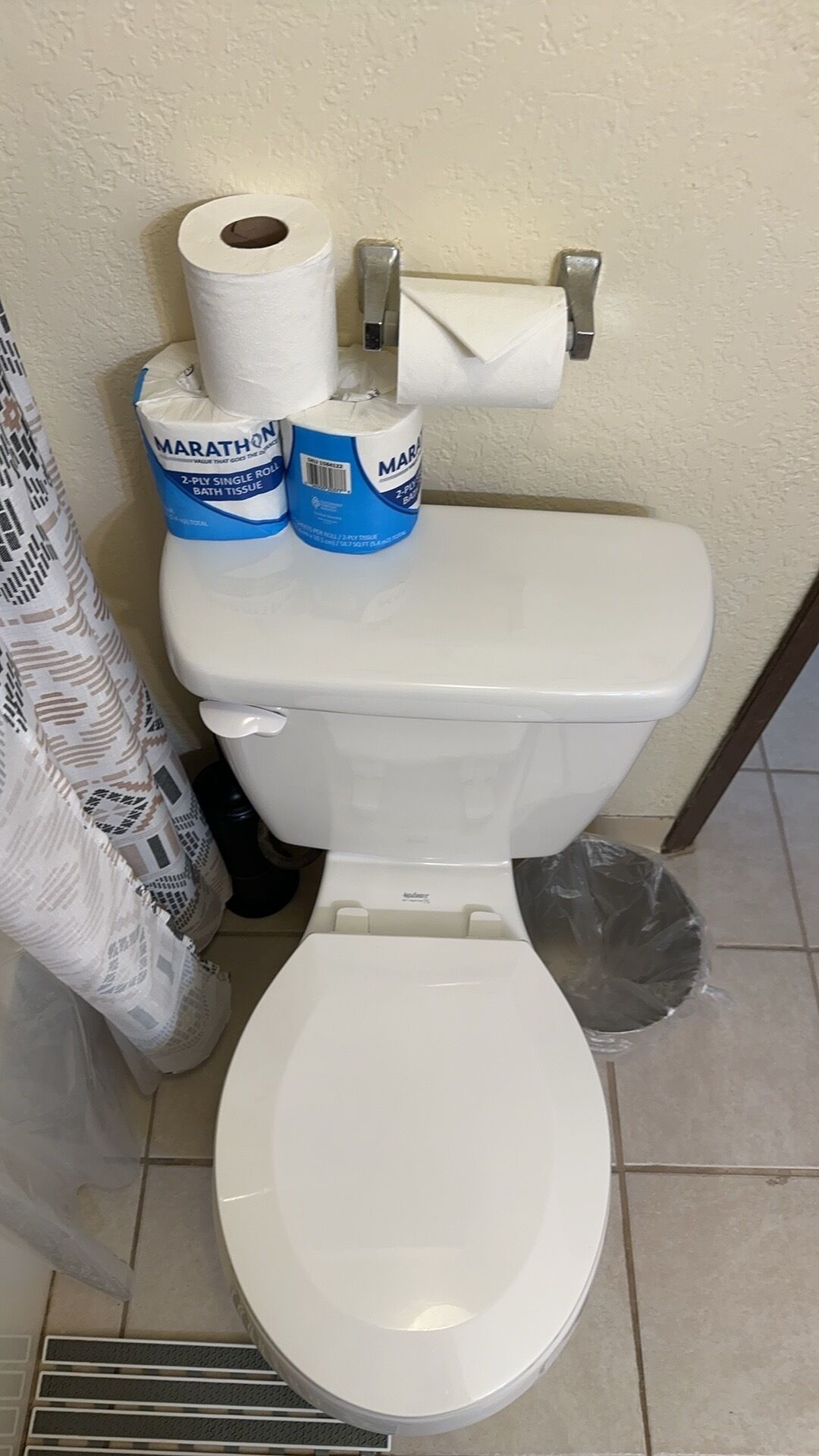 A toilet with two rolls of toilet paper and a trash bin.