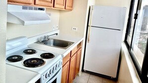 A compact kitchen with wooden cabinets, a white stove, a sink, and a refrigerator.
