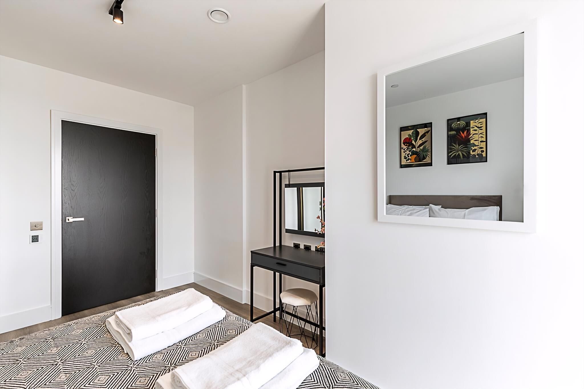 A hotel room with a bed, a desk with a chair, a mirror, and two wall-mounted artworks.