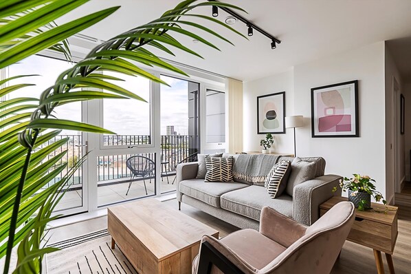A modern living room with a sofa, coffee table, and a view of the city through large windows.