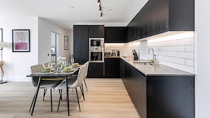Una cocina moderna con armarios oscuros, una isla central y un comedor con mesa dispuesta para cuatro.