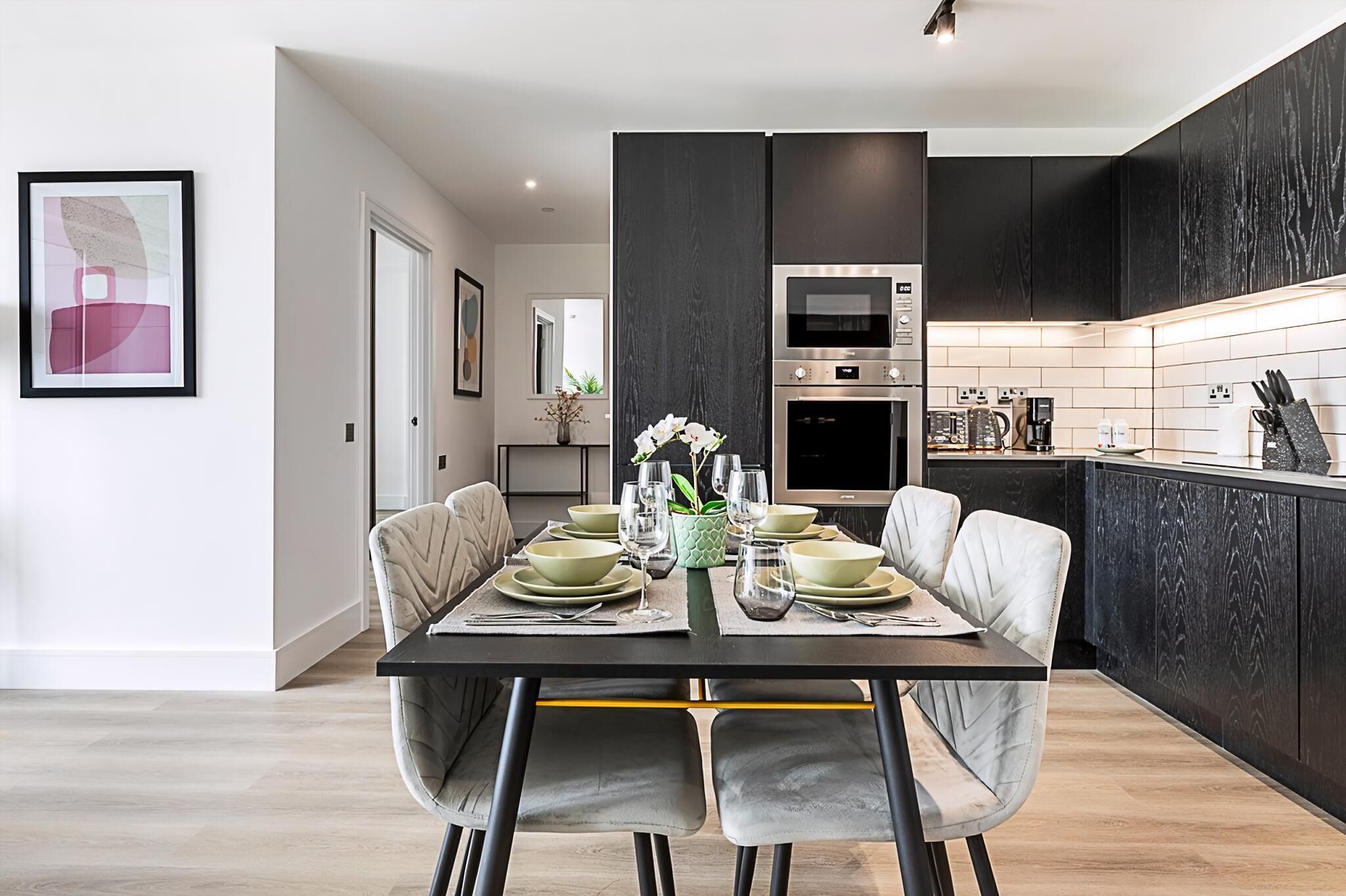 A modern kitchen with dark cabinetry, a central island, and a dining area with a set table.