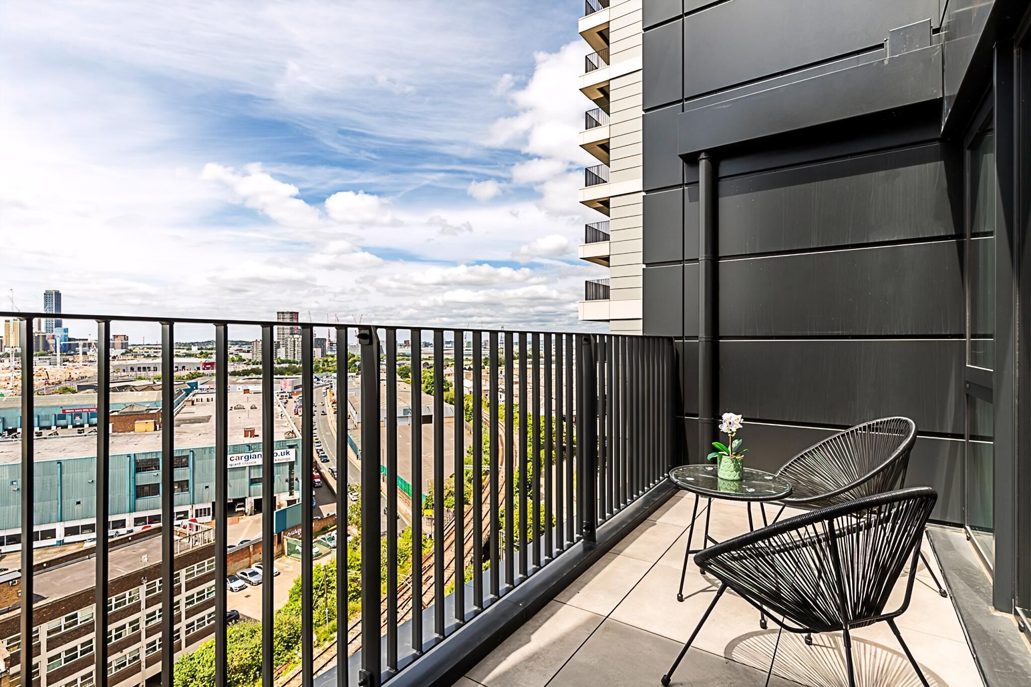 A balcony with a view of a cityscape, a small table with chairs, and a potted plant.