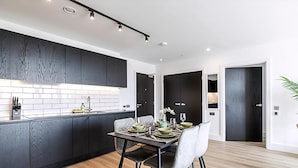 Una cocina moderna con armarios oscuros, un protector contra salpicaduras de azulejos y una zona de comedor con una mesa preparada para cuatro.
