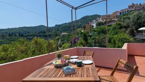 Ein Holztisch gedeckt mit Tellern, Schüsseln und einem Buch auf einer Terrasse mit Blick auf eine Hügellandschaft.