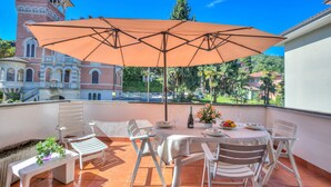 A terrace with a table, chairs, and an umbrella. - Appartamento Gaya Stresa Center (Stresa)