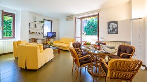 A living room with a yellow sofa, wicker chairs, a glass coffee table, a TV, and a bookshelf. - Appartamento Gaya Stresa Center (Stresa)