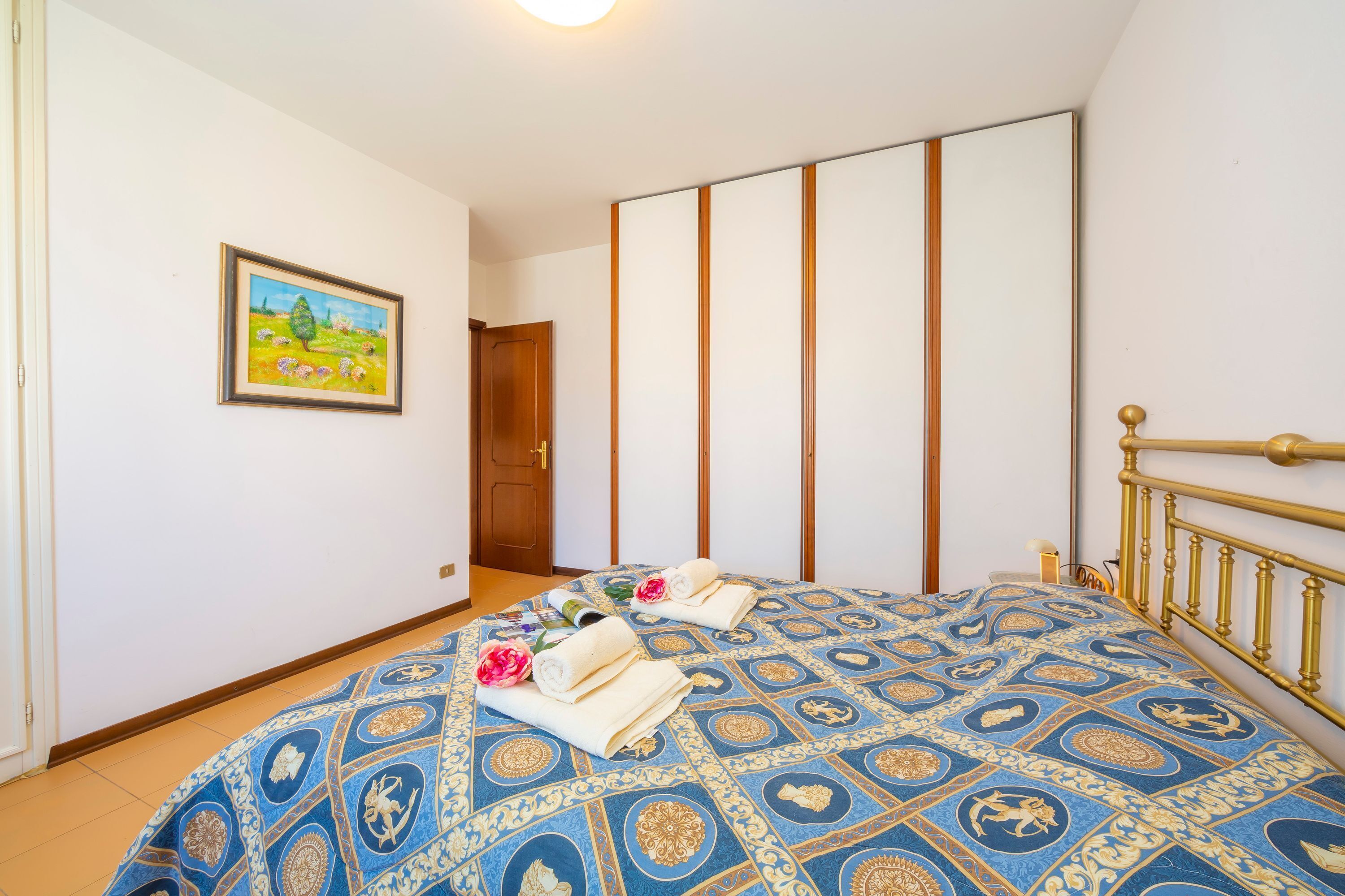 A bedroom with a bed, a wooden door, a painting, and a wardrobe.