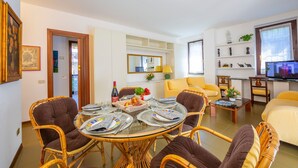 A dining area with a round glass table, wicker chairs, and a yellow sofa. - Appartamento Gaya Stresa Center (Stresa)