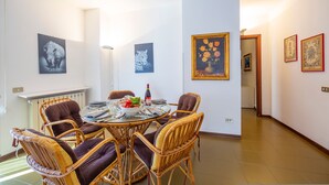 A dining area with wicker chairs and a round table, white walls, and framed artwork. - Appartamento Gaya Stresa Center (Stresa)
