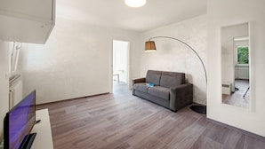 Ein modernes Wohnzimmer mit grauem Sofa, einem Flachbildfernseher und einer Lampe.