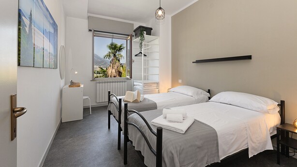 Een moderne hotelkamer met twee bedden, een raam met uitzicht op palmbomen, een witte kledingkast en een schilderij aan de muur.